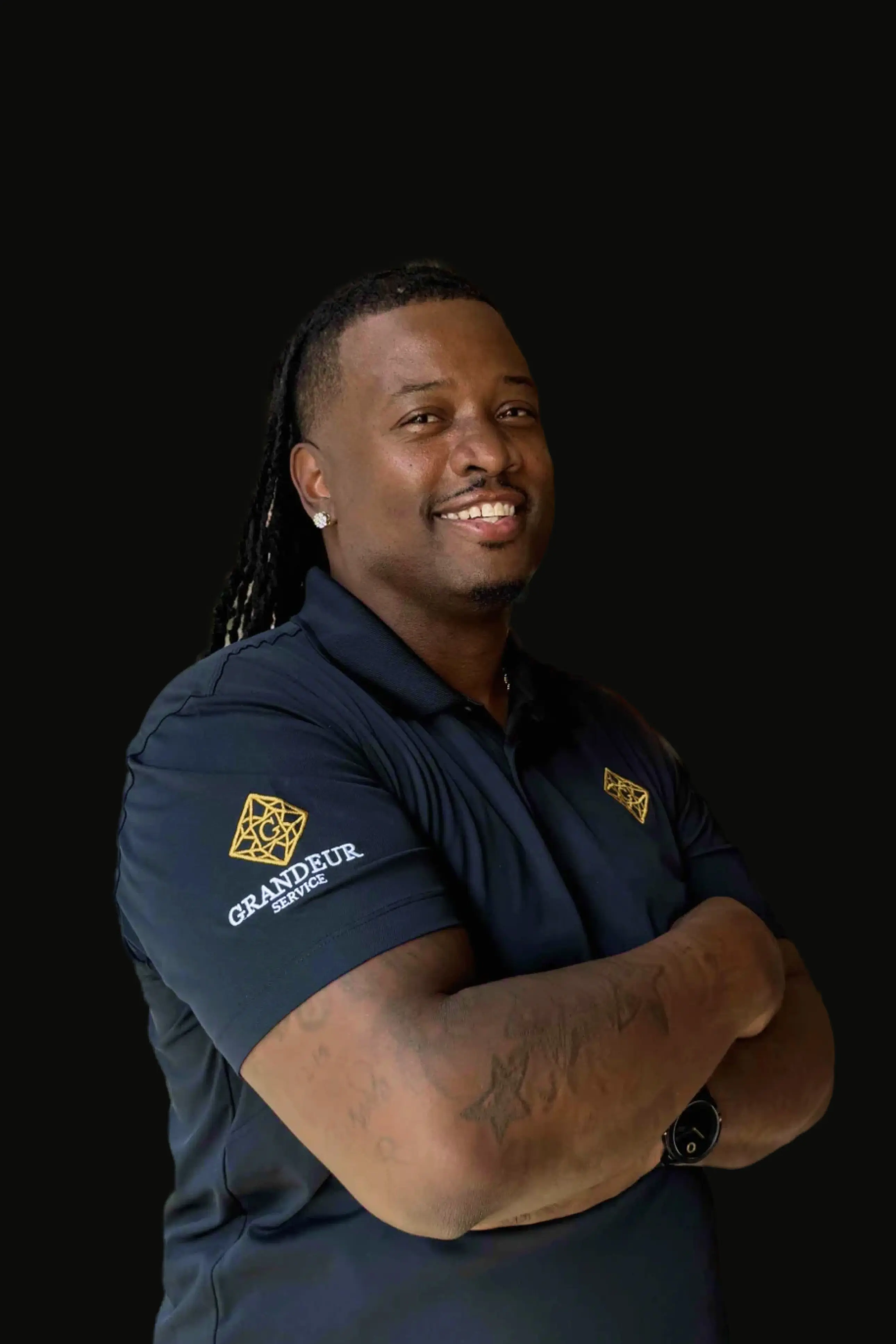 a middle-aged black man with a goatee wearing and dreadlocks wearing Grandeur Service polo shirt