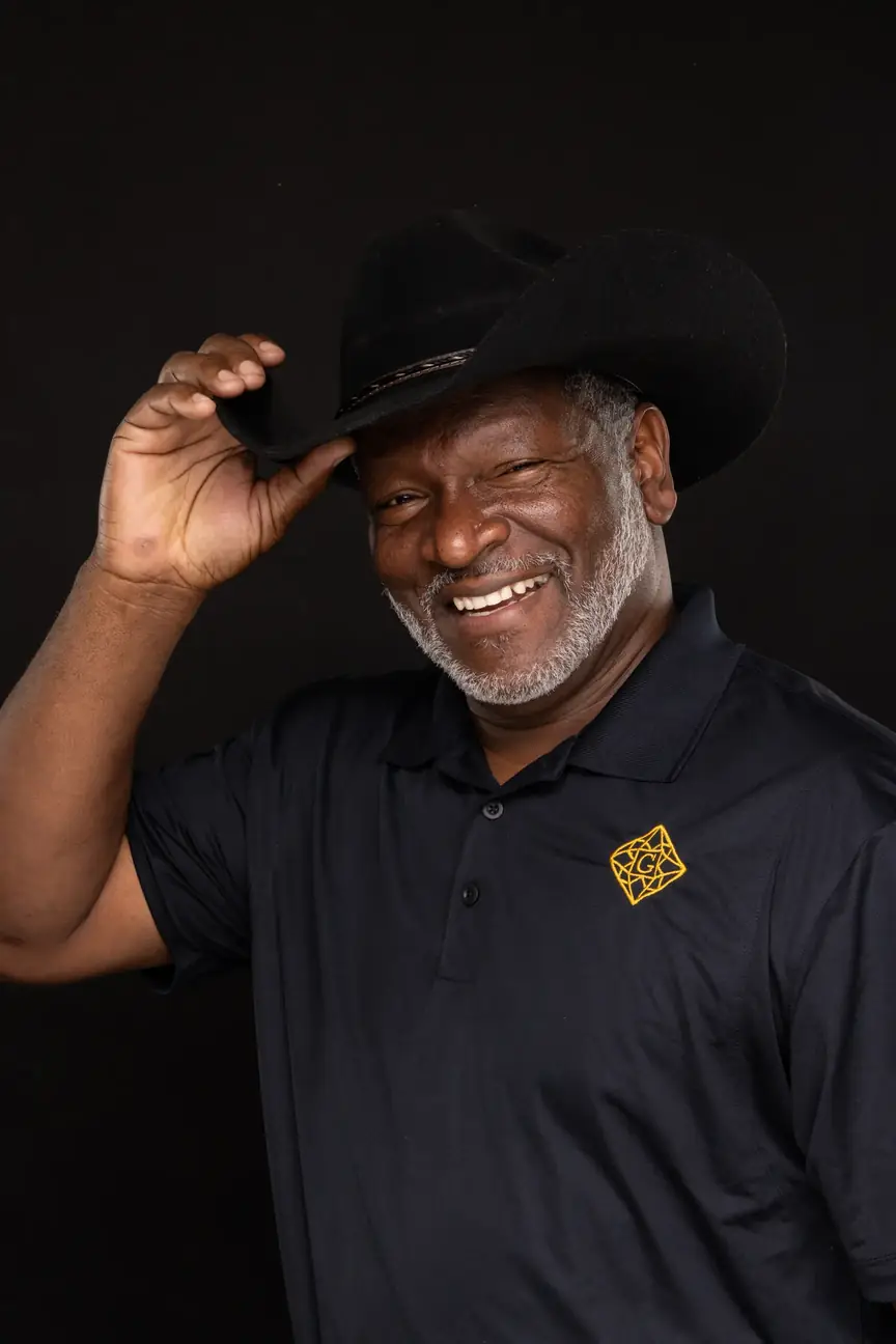 older black man, smiling, with a trimmed grey beard tipping his cowboy hat